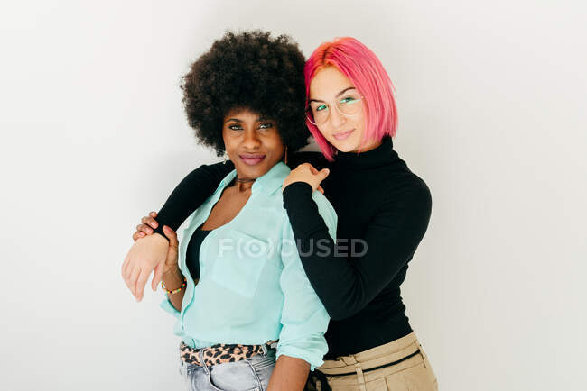 Fröhliche junge Frau mit rosa Haaren und afroamerikanische Freundin in stilvollem Outfit, während sie gemeinsam Spaß auf weißem Hintergrund haben — Stockfoto