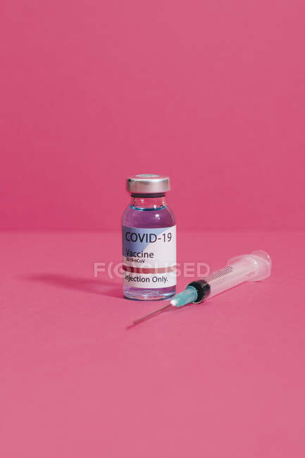 Fiole de vaccin contre le coronavirus près de la seringue avec aiguille sur fond rose — Photo de stock
