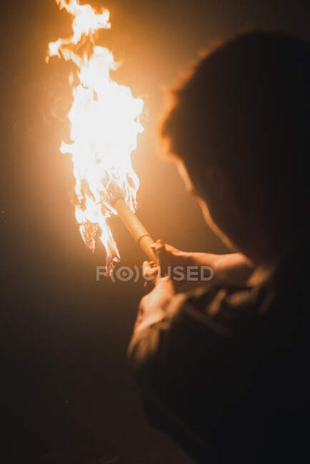 Back view of cropped anonymous male speleologist with flaming torch standing in dark narrow rocky cave while exploring subterranean environment — Stock Photo