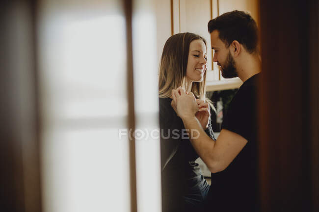 Cheerful bearded man hugging smiling woman while leaning on cupboard with sink in cozy kitchen at home — Stock Photo