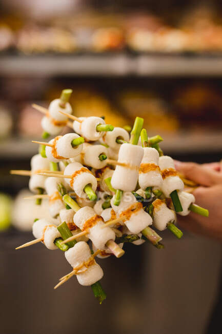 Manos sosteniendo apetitosas brochetas vegetarianas saludables preparadas con verduras y frutas en el restaurante - foto de stock