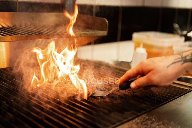 Crop chef masculino anônimo grelhar saborosa Patty enquanto prepara hambúrgueres na cozinha do restaurante — Fotografia de Stock