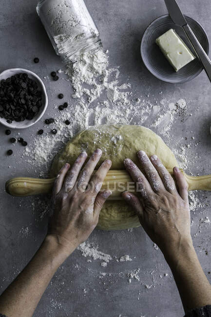 Рука неузнаваемой женщины с помощью деревянного инструмента катит свежее тесто для выпечки на уютной кухне — стоковое фото