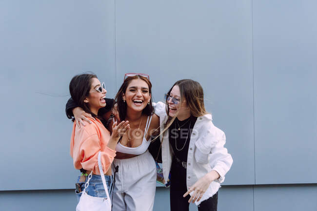 Positive female friends in trendy sunglasses and casual clothes laughing happily while spending pleasant time together — Stock Photo