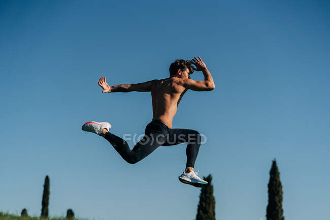 Вид збоку активного спортсмена-чоловіка в спортивному одязі, стрибки під час кардіо-тренувань на сонячному світлі — стокове фото