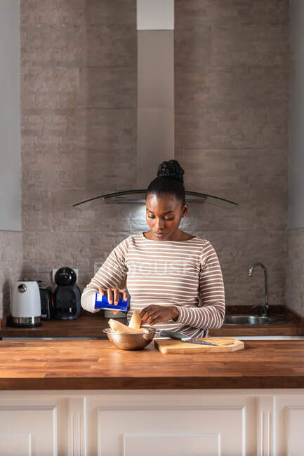 Young African American female salting plantains in bowl while preparing patacones at table in house — Stock Photo