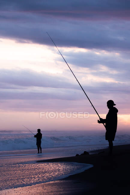 Силуэт рыбаков на берегу моря на закате — стоковое фото