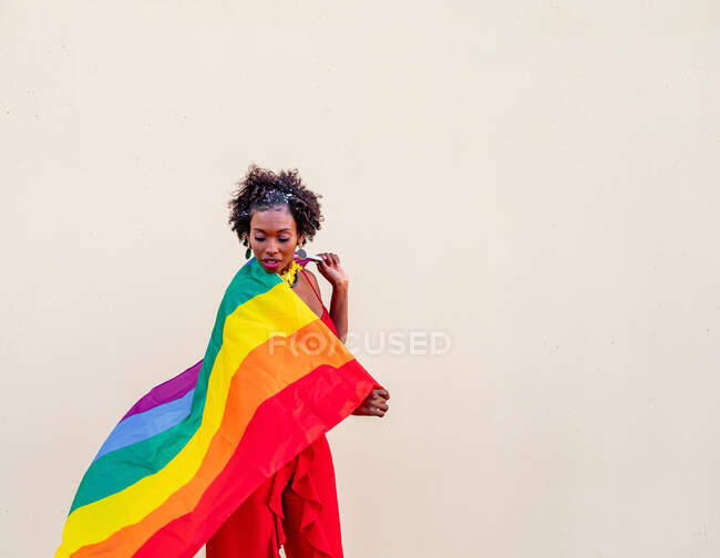 Stylish African American female in trendy clothes with colorful flag looking down during celebration — Stock Photo