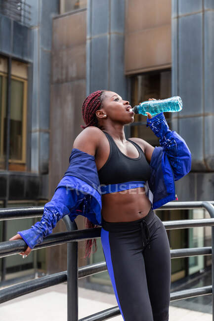 Sportlerin stützt sich auf Zaun und hält Flasche — Stockfoto