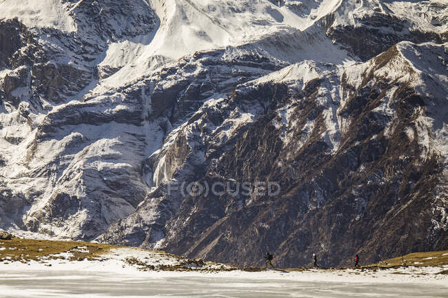 Удаленный обзор компании туристов, идущих по заснеженной местности на фоне Гималайских гор во время похода зимой в Непале — стоковое фото