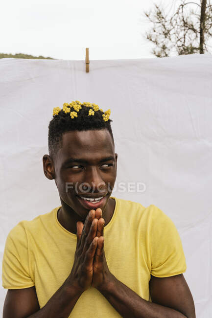 Bonito sorriso afro-americano masculino com flores amarelas no cabelo olhando para o fundo branco — Fotografia de Stock