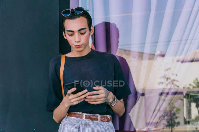 Low angle of gay male messaging on social media on mobile phone while standing in street and smiling — Stock Photo