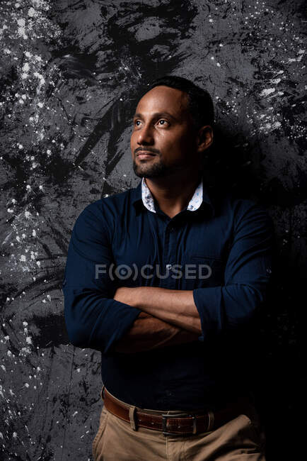 Serious stylish ethnic male standing on dark background looking away — Stock Photo