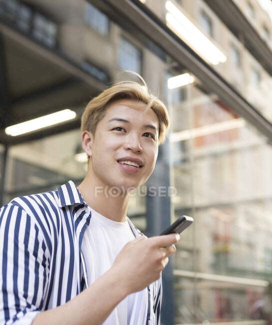Content ethnic male with blond hair standing in street and browsing mobile phone while looking at camera — Stock Photo