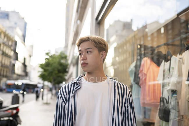 Handsome ethnic male model with blond hair and in stylish outfit standing in street and looking away — Stock Photo