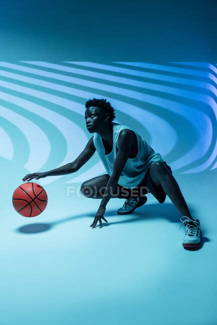 Schwarze Frau mit Basketballoutfit im Studio mit Farbgelen und Projektorlichtern vor blauem Hintergrund — Stockfoto