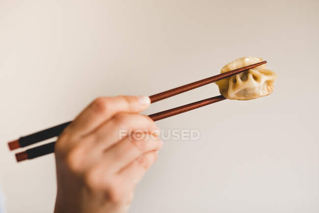 Mano de mujer sosteniendo palillos con sabroso dumpling al vapor sobre fondo gris - foto de stock