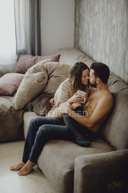 Щасливий чоловік і жінка з чашкою гарячого напою посміхаються і дивляться один на одного, проводячи час вдома вранці — стокове фото