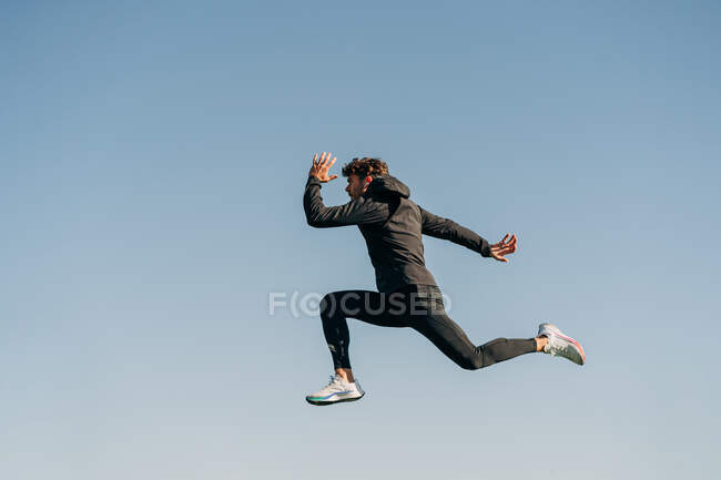 Вид сбоку активного спортсмена в спортивной одежде, прыгающего во время кардиотренировки при солнечном свете — стоковое фото