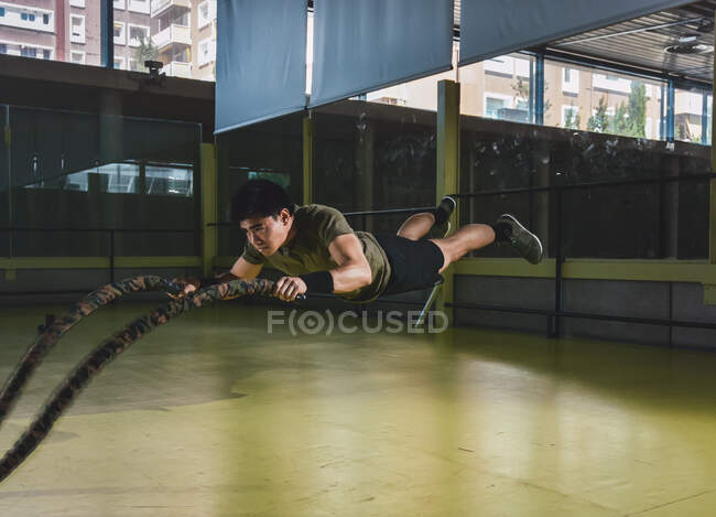 Focused Asian boy training with battle rope in modern crossfit gym — Stock Photo