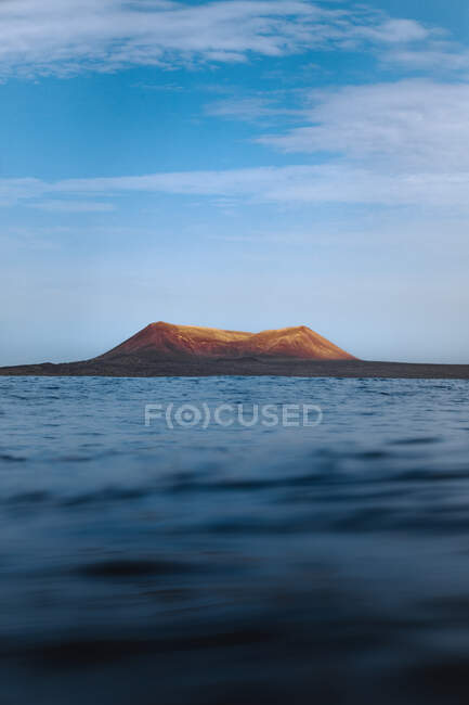 Blaues Meer wogt über die Küste in der Nähe eines fernen Berges — Stockfoto