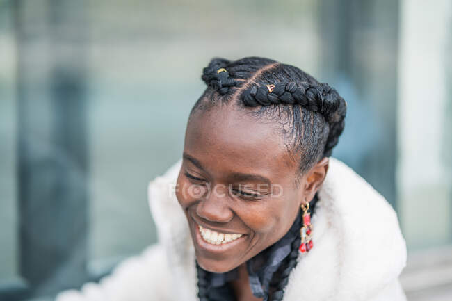 Stylish happy beautiful African American lady with African braids seriously looking down in park — Stock Photo