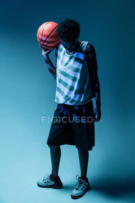 Чорна жінка з баскетбольним вбранням в студії з використанням кольорових гелів і проекторних вогнів на синьому фоні — стокове фото