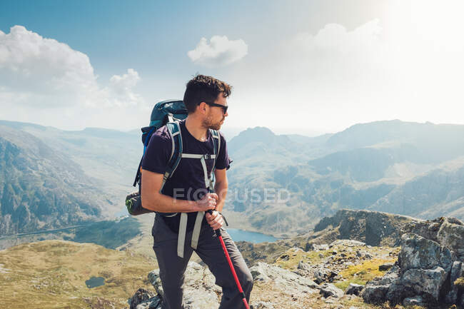 Viajando hombre senderismo en las montañas con bastón de trekking durante las vacaciones en verano en Gales - foto de stock