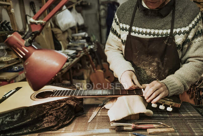 Обрізати анонімного чоловіка-лютьє в светрі вимірюючи горіх при ремонті акустичної гітари на майстерні — стокове фото