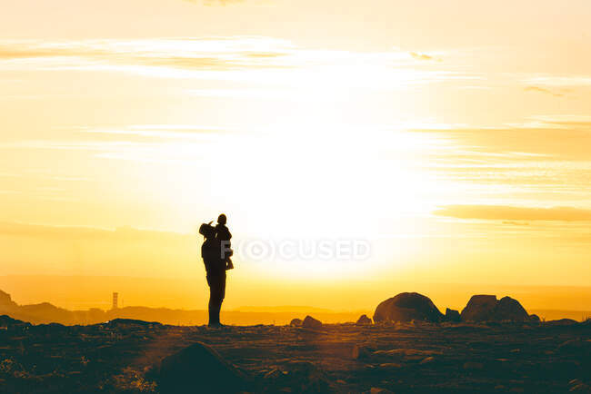 Seitenansicht eines anonymen Mannes, der ein Kind in der Luft hält, im felsigen rauen Tal bei Sonnenuntergang — Stockfoto