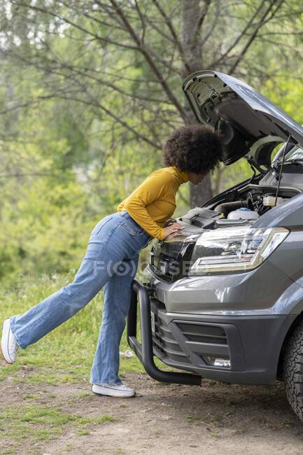Seitenansicht einer Afroamerikanerin, die Kühlmittelbehälter öffnet und kaputte Lieferwagen während einer Autofahrt in der Landschaft repariert — Stockfoto