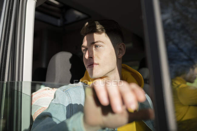 Молодой человек смотрит в окно во время езды на современном автомобиле во время дорожной поездки в выходные — стоковое фото