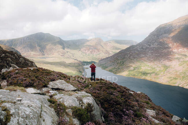 Blick zurück auf anonyme Männer, die Hügel und Fluss bewundern, während sie auf rauen Hängen während einer Reise durch Snowdonia, UK, stehen — Stockfoto