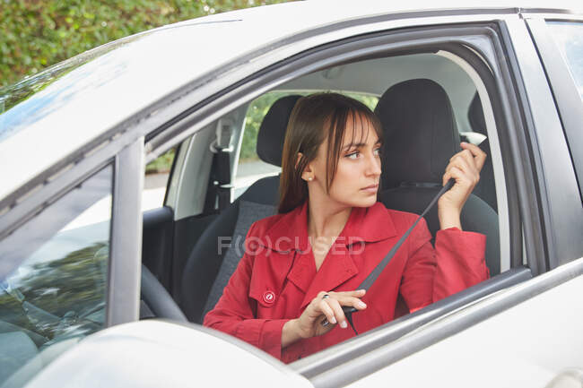 Vista lateral de la joven conductora en la chaqueta roja de moda abrochando el cinturón de seguridad mientras se prepara para el viaje dentro del automóvil moderno - foto de stock