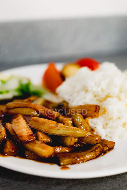 Primer plano de la deliciosa berenjena Yuxiang cocida con verduras saludables y arroz en el plato blanco en el restaurante asiático - foto de stock
