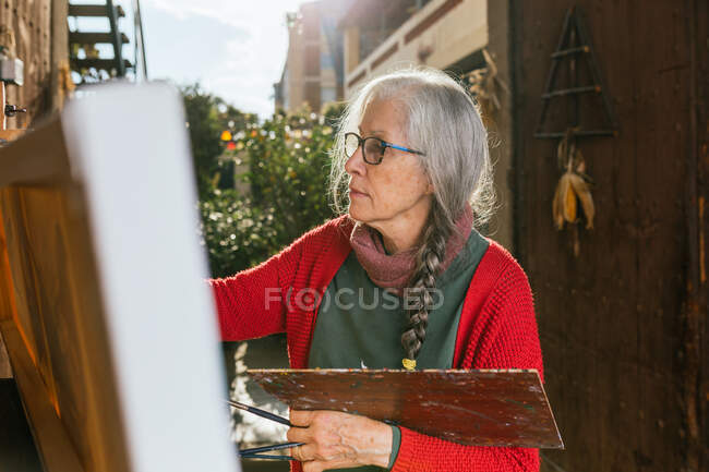Vista lateral de artistas idosas em máscara protetora pintura em tela no quintal no dia ensolarado no verão — Fotografia de Stock