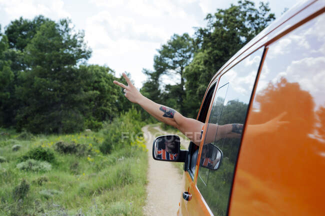 Урожай анонимный путешественник вождение фургон на дороге в лесу и показ знак мира во время летней поездки — стоковое фото