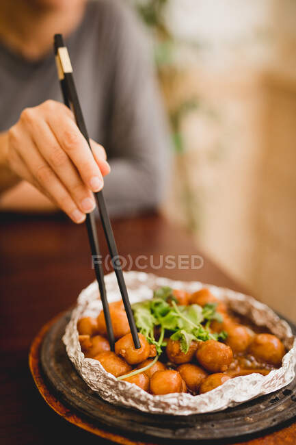 Female sitting in Asian cafe and eating prepared appetizing taro in foil with chopsticks — Stock Photo