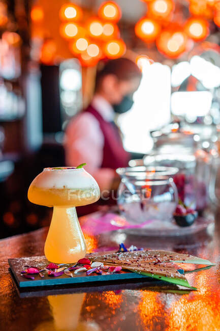 Sour cocktail with mint leaf in mushroom shaped glass served on wooden counter with bottle of alcohol drink in pub — Stock Photo