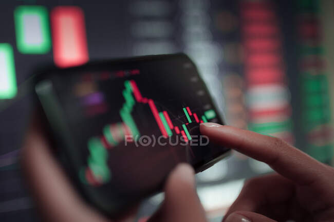 Faceless crop broker using mobile phone while working with financial chart during trading — Stock Photo