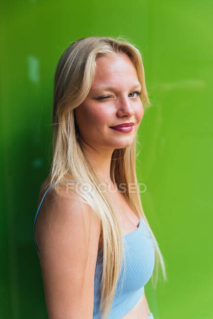 Vista laterale della femmina civettuola con i capelli biondi che strizzano l'occhio alla fotocamera su sfondo verde — Foto stock