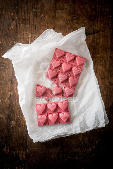 Composición minimalista vista superior con piezas de chocolate rosa hecho a mano con diseño en forma de corazón sobre fondo de madera - foto de stock