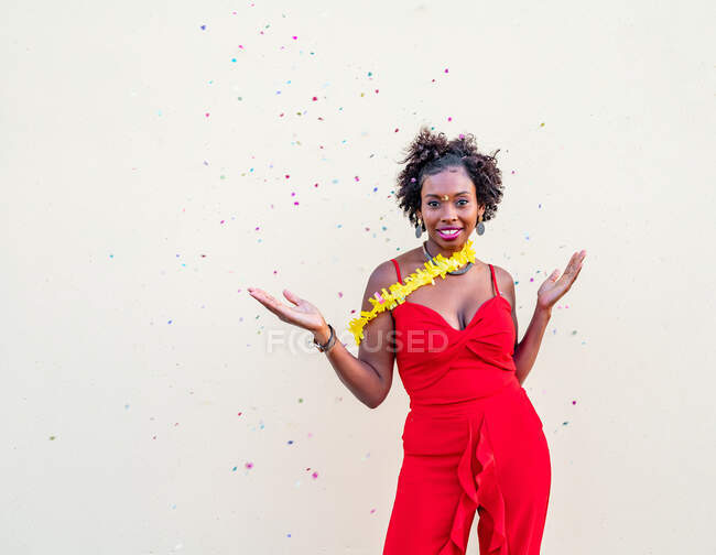 Emocionada mujer afroamericana con los brazos extendidos y la boca abierta de pie bajo la caída de confeti en el evento contra el fondo blanco - foto de stock
