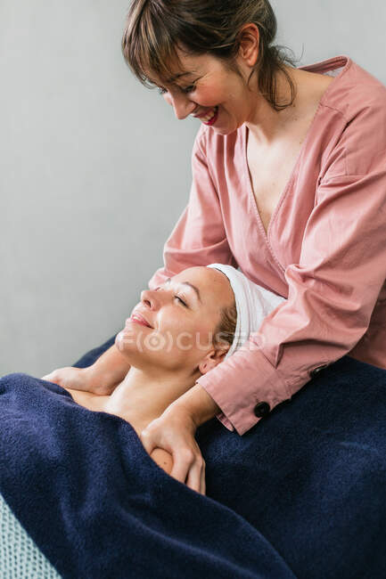 Contenido masajista masajeando hombros de cliente femenino acostado en la mesa en salón de belleza - foto de stock