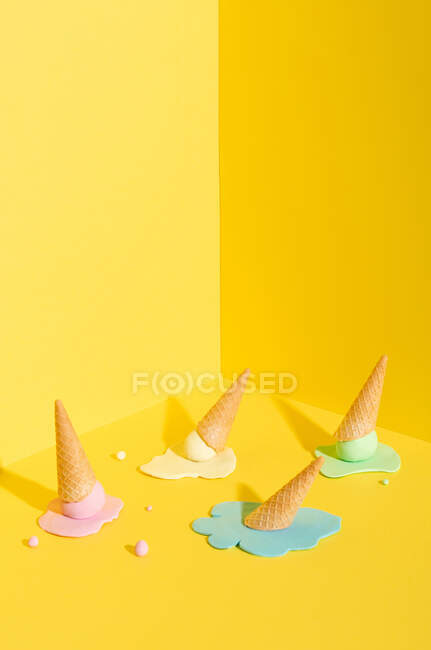 Helado de fusión azul, amarillo y rosa burlón en cono de gofre colocado sobre fondo amarillo que representa el concepto de verano - foto de stock