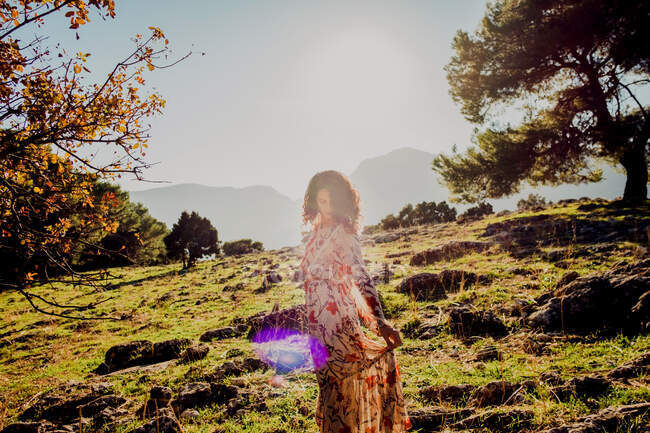 Carefree female in summer dress standing on rocky hill in highlands on sunny day — Stock Photo