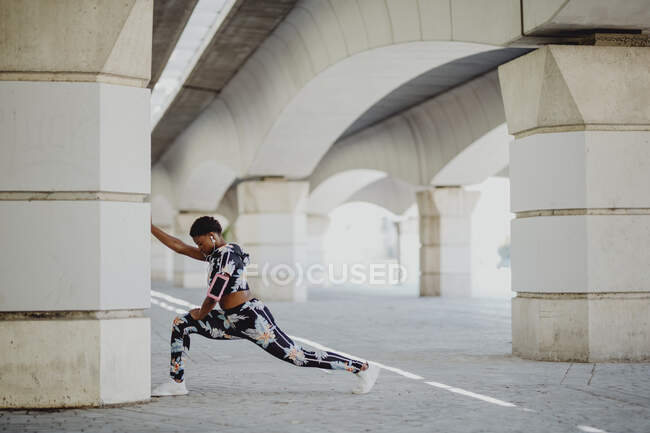 Joven fitness mujer afroamericana estirando las piernas antes de correr en la calle de la ciudad - foto de stock