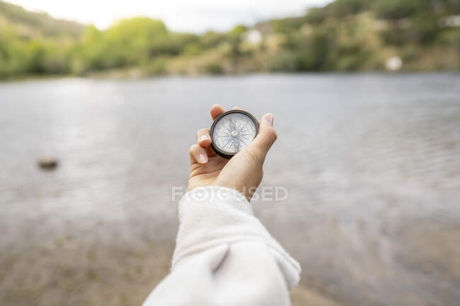 Mulher irreconhecível usando bússola retro para navegar no campo no fundo borrado do rio — Fotografia de Stock