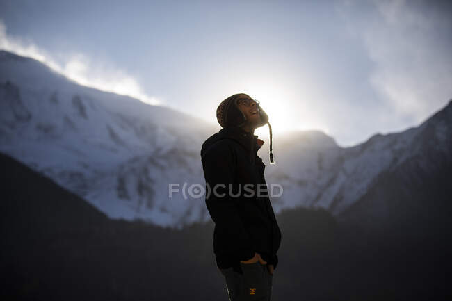 Вид сбоку улыбающегося мужчины в теплой одежде, стоящего на фоне горного хребта Фалайя в солнечный день в Непале — стоковое фото