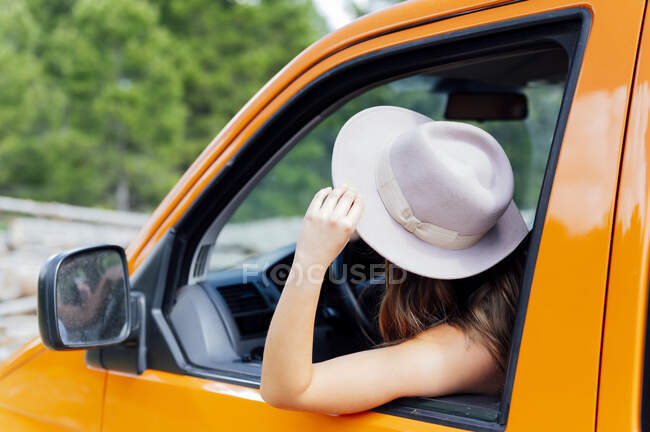 Side view of female traveler sitting on driver seat in van and enjoying road trip in summer — Stock Photo